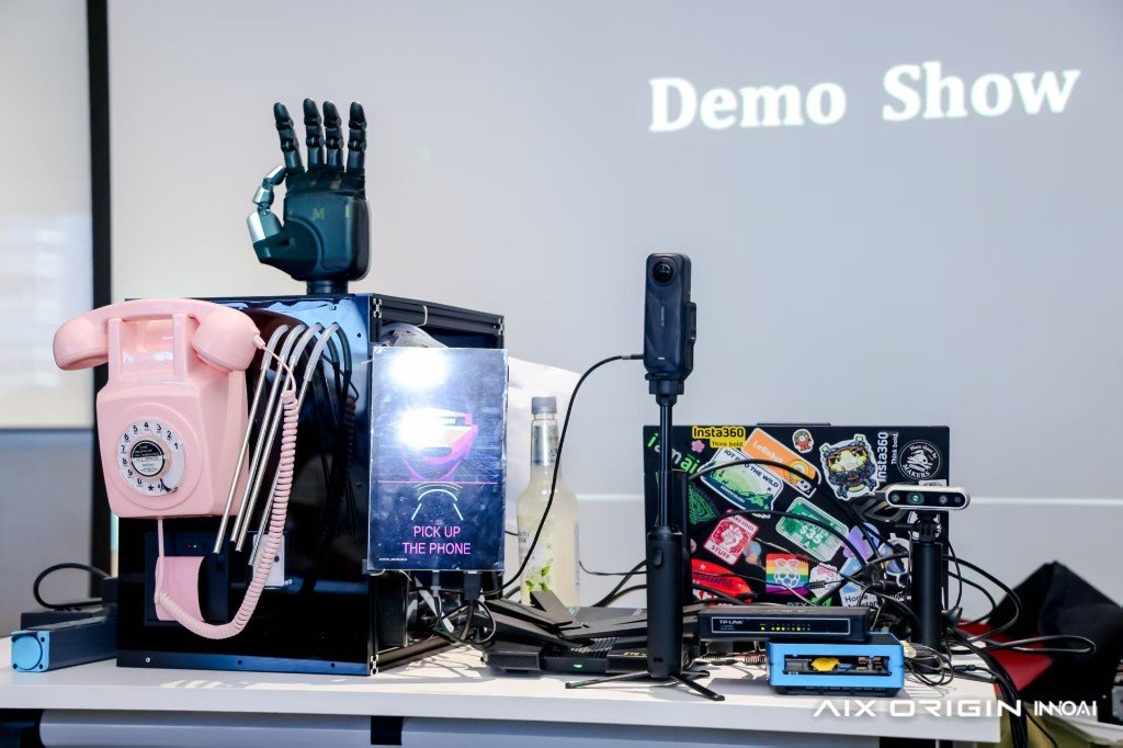 PΛN 展台：粉色转盘电话、"PICK UP THE PHONE"、Insta360 X5、RealSense、TP-Link 交换机，和站在机箱顶上的 Apex 灵巧手