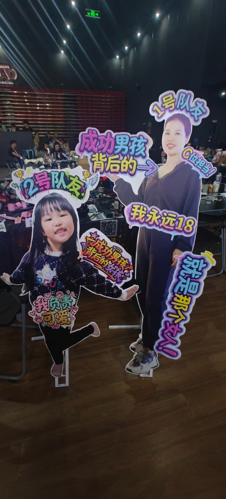 两块真人大小的 KT 板队友 — 1 号队友（妻子，C 位担当），2 号队友（女儿，成功男孩背后的 C 位担当）